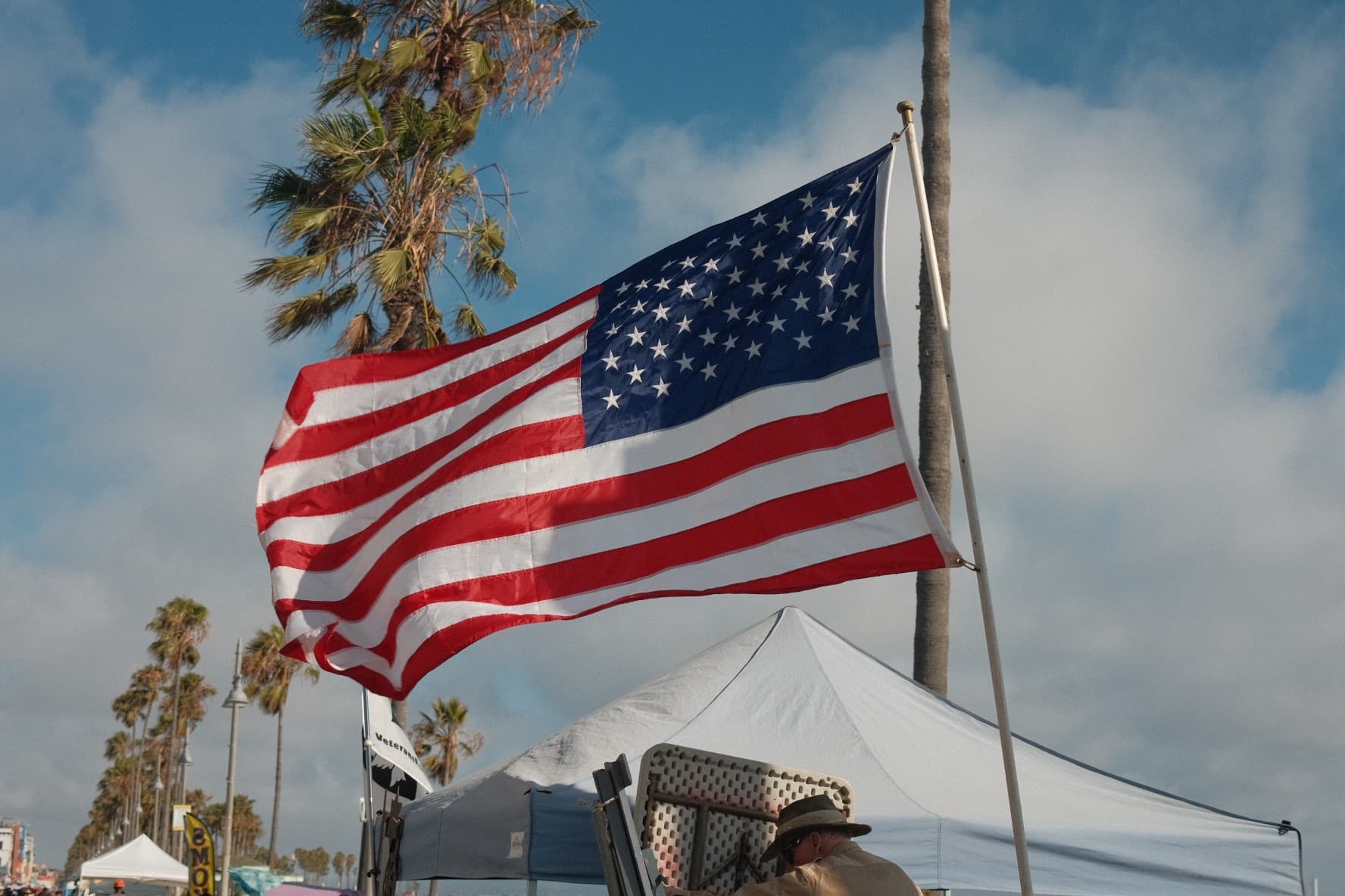 An American flag flying over a beach boardwalk lined with palm trees
