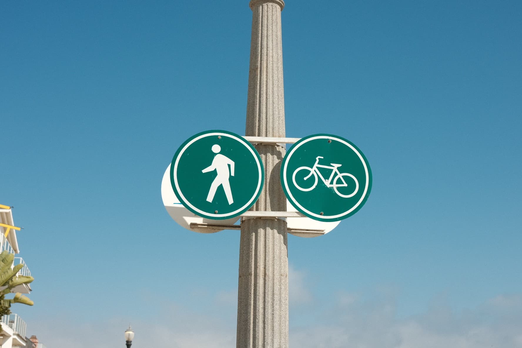 Pedestrian and bike path signs on a stone column against a blue sky