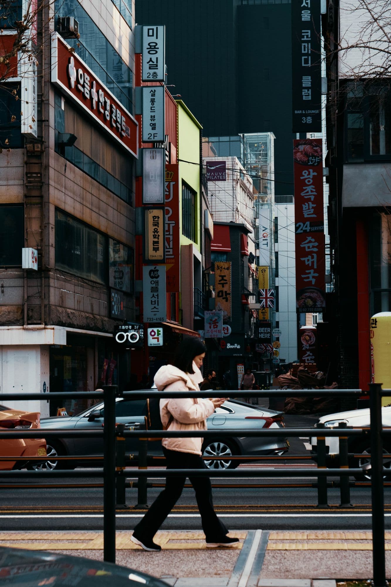 A woman in a pink puffer jacket walking past a street of Korean signs in Seoul